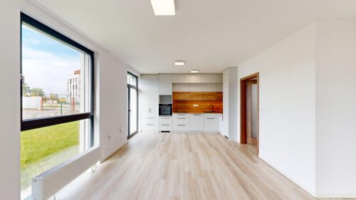 Bright open-plan kitchen with white cabinets and wood backsplash, large windows, and light wood flooring inside a modern home.