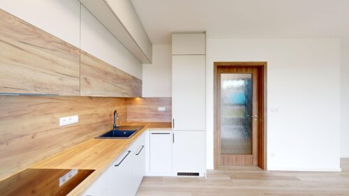 Modern kitchen with light wood countertops and white flat-panel cabinets, and a wooden door with frosted glass.