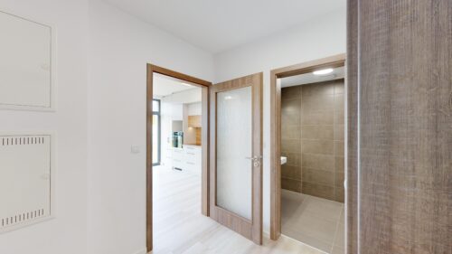 Bright hallway with wooden-framed doors; view into a white kitchen and a tiled bathroom.