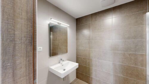 Modern bathroom with a wall-mounted white sink, rectangular mirror, and brown tiled wall on the right side.
