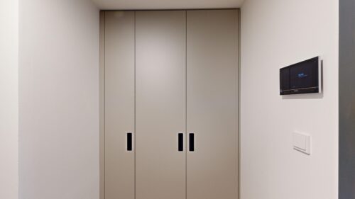 Beige elevator doors with vertical black handles in a white hallway; a wall-mounted display is on the right side.