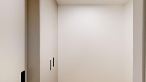 Inside a modern elevator car with light beige walls and closed metal doors along the left side.