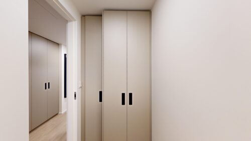 Narrow hallway with tall beige built-in cabinets and black vertical handles along the right wall.