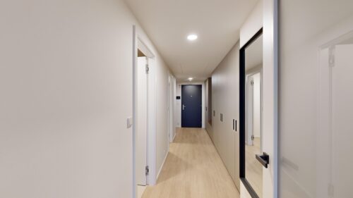 Bright hallway with white walls and built-in cabinets on the right, leading to a dark blue front door at the end.