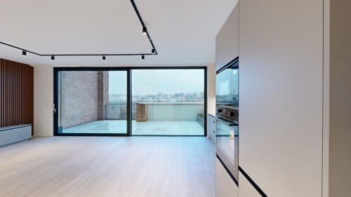Modern kitchen with built-in ovens on the right and large sliding glass doors to a balcony overlooking the city skyline.