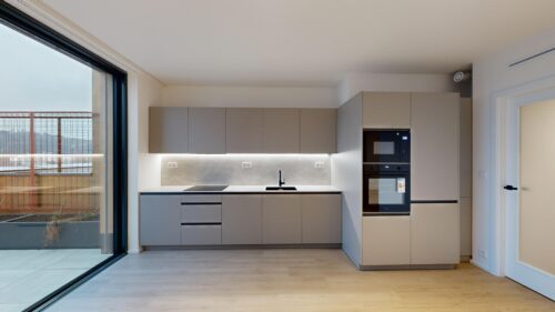 Modern kitchen with matte gray cabinets, integrated sink, and a large sliding glass door opening to a balcony outdoorsy area.