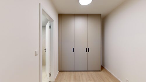 Narrow hallway with a tall beige wardrobe at the end and light wood flooring.