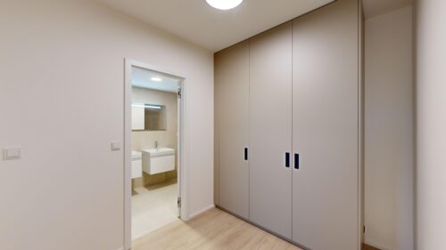 Hallway with tall beige cabinets along the right and an open bathroom doorway showing a sink and mirror on the left.