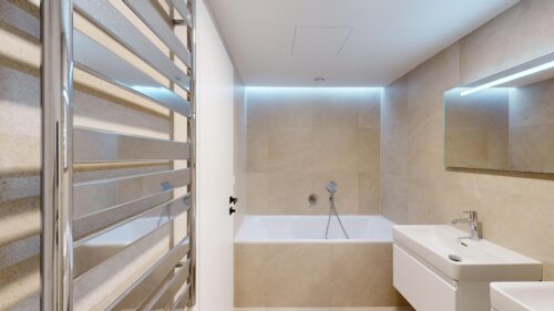 Modern bathroom with beige tile walls, a white built-in bathtub, chrome towel warmer on the left, and a wall-mounted sink with a mirror.