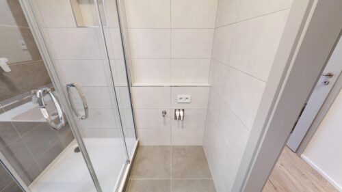 Shower enclosure with glass doors and chrome handles in a tiled bathroom, view of wall tiles and floor grout lines.