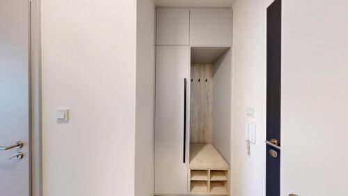 Open built-in wardrobe with tall gray cabinets, an alcove with hooks and a small bench with cubby shelves.