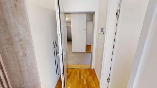 Open doorway into a bright hallway with white walls and numbered room 411 on the inner wall, wooden floor visible beyond.