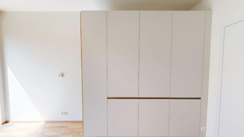 Tall gray built-in wardrobe with multiple vertical doors in a bright room with a wooden floor.