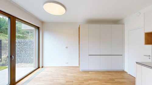 Bright modern kitchen with white handleless cabinets, light wood floors, and a large glass sliding door to the garden outside.