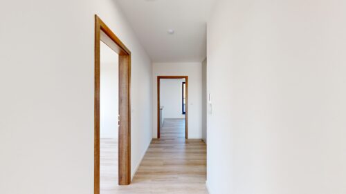 Bright hallway with light wood flooring and white walls, open doors framed in wood. (Interior of a modern home)