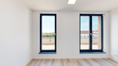 Bright empty room with two tall black-framed glass doors opening to a balcony and blue sky outside.