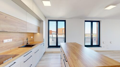 Bright modern kitchen with white cabinets, wood countertops, and large glass doors opening to a balcony.