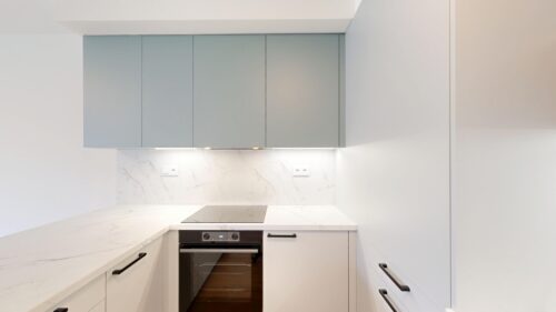 Modern minimalist kitchen with white marble countertops, gray upper cabinets, and a built-in oven beneath a glass-ceramic cooktop