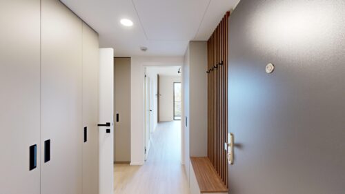 Bright hallway with white built-in wardrobes on the left and a wooden slat divider on the right, leading to a sunlit room at the end.
