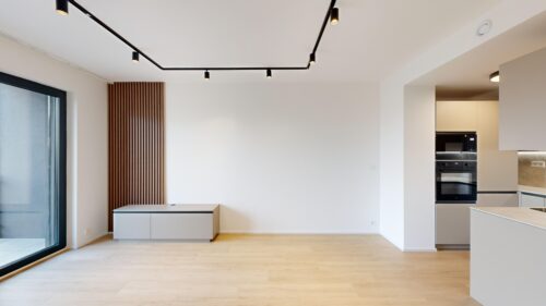 Minimalist kitchen with white walls, light wood floor, vertical wooden slat feature, and built‑in stainless steel oven on the right.