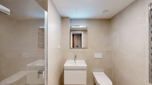 Modern beige-tiled bathroom with a wall-mounted sink, mirror, toilet, and glass shower enclosure.