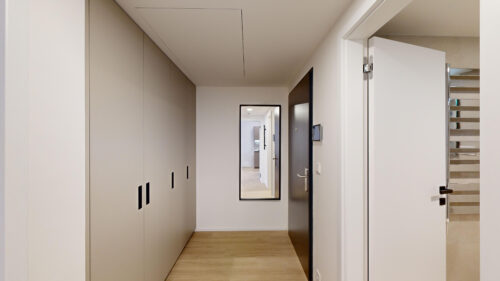 Hallway with tall gray built-in closets on the left, white walls, and an open door leading to stairs on the right.