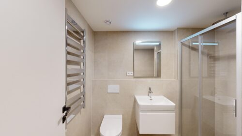 Modern bathroom with a wall-mounted sink, rectangular mirror, and wall-hung toilet amid beige tiled walls.