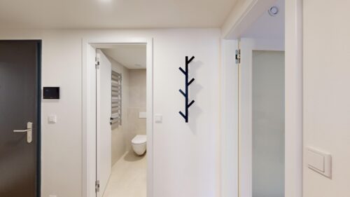 White hallway with an open bathroom door showing a toilet and a metal towel rack against beige tiles inside
