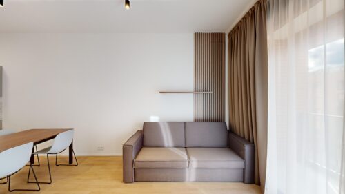Bright, minimalist living area with a gray sofa, wooden slat accent wall, and sheer white curtains by a large window
