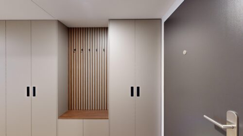 Row of light gray lockers with black handles, centered by vertical wooden slats and a built-in bench in a gray hallway