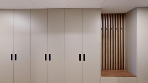 Row of beige storage cabinets with black handles, and a wooden slatted wall panel on the right.