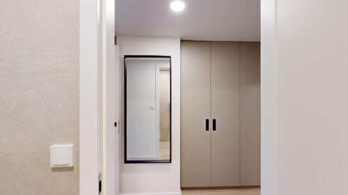 White hallway with a tall black-framed mirror on the left and beige built-in wardrobes on the right.