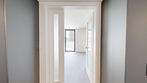 Series of white door frames creating a tunnel view toward a bright room with a glass door to a balcony outside.