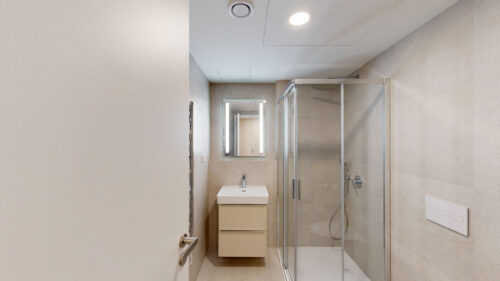 Modern beige bathroom featuring a glass-framed shower, a wall-mounted sink, and a mirrored cabinet with vertical lighting assets above the basin.