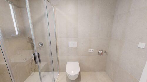 Contemporary bathroom with glass shower enclosure, wall-mounted toilet, and beige tiled walls and floor.