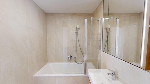 Modern bathroom featuring a bathtub with a glass shower enclosure and beige tiled walls.