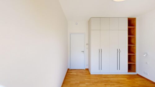 Bright corner of a minimalist room with white built-in wardrobes and wooden open shelves on the right, oak floor.