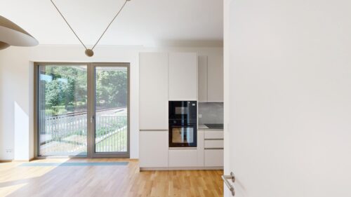 Bright modern kitchen with white cabinets, built-in oven and microwave, and a glass door opening to a sunny balcony outside.