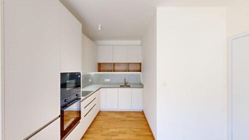 Modern, white kitchen with tall cabinets, built-in oven and induction hob, on a warm wood floor.