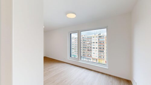 Empty white room with light wood floor and a large window overlooking city apartment buildings?