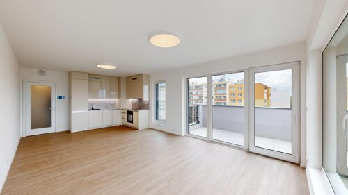 Bright open-plan kitchen and living area with large glass doors to a balcony and city buildings outside